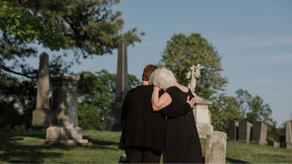 Two women in black embracing at a cemetery